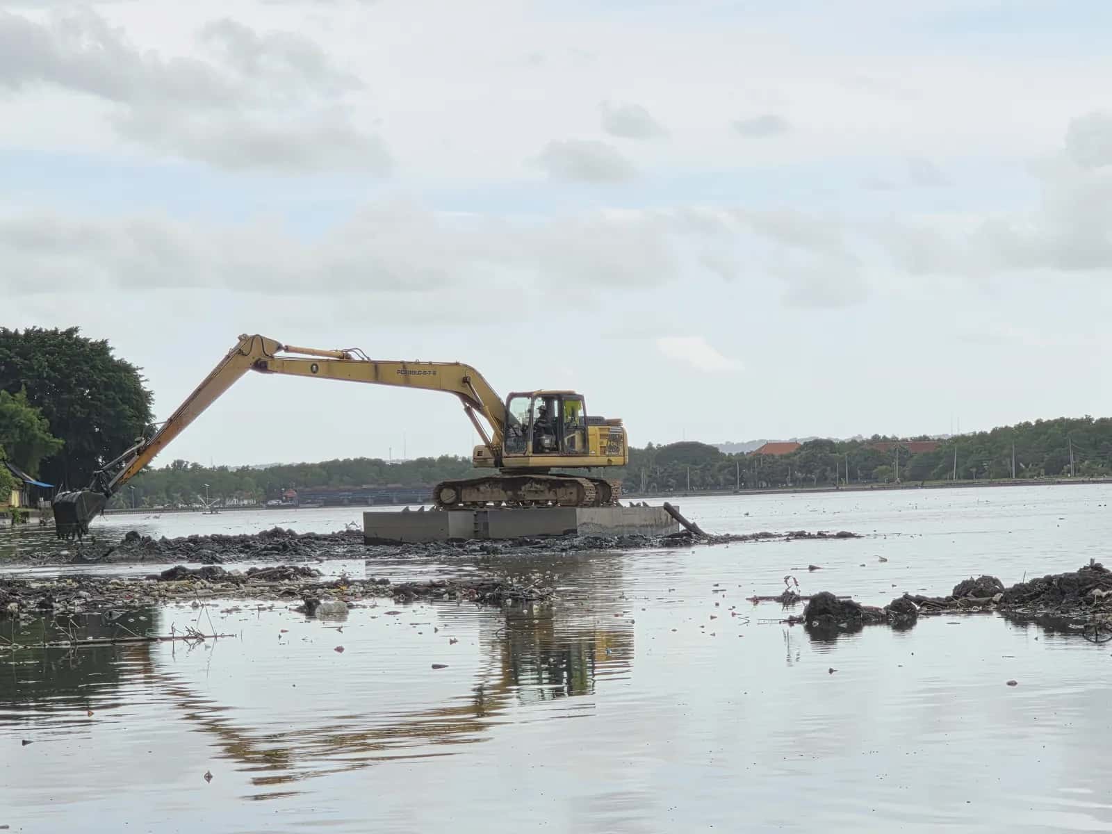 Excavator Komatsu PC200 berlengan panjang bekerja di atas pondasi apung di area perairan