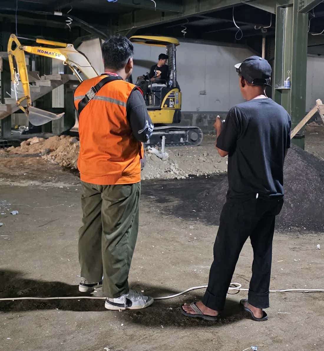 Mini excavator Komatsu PC30MR bekerja di dalam bangunan berstruktur baja sementara dua orang mengawasi