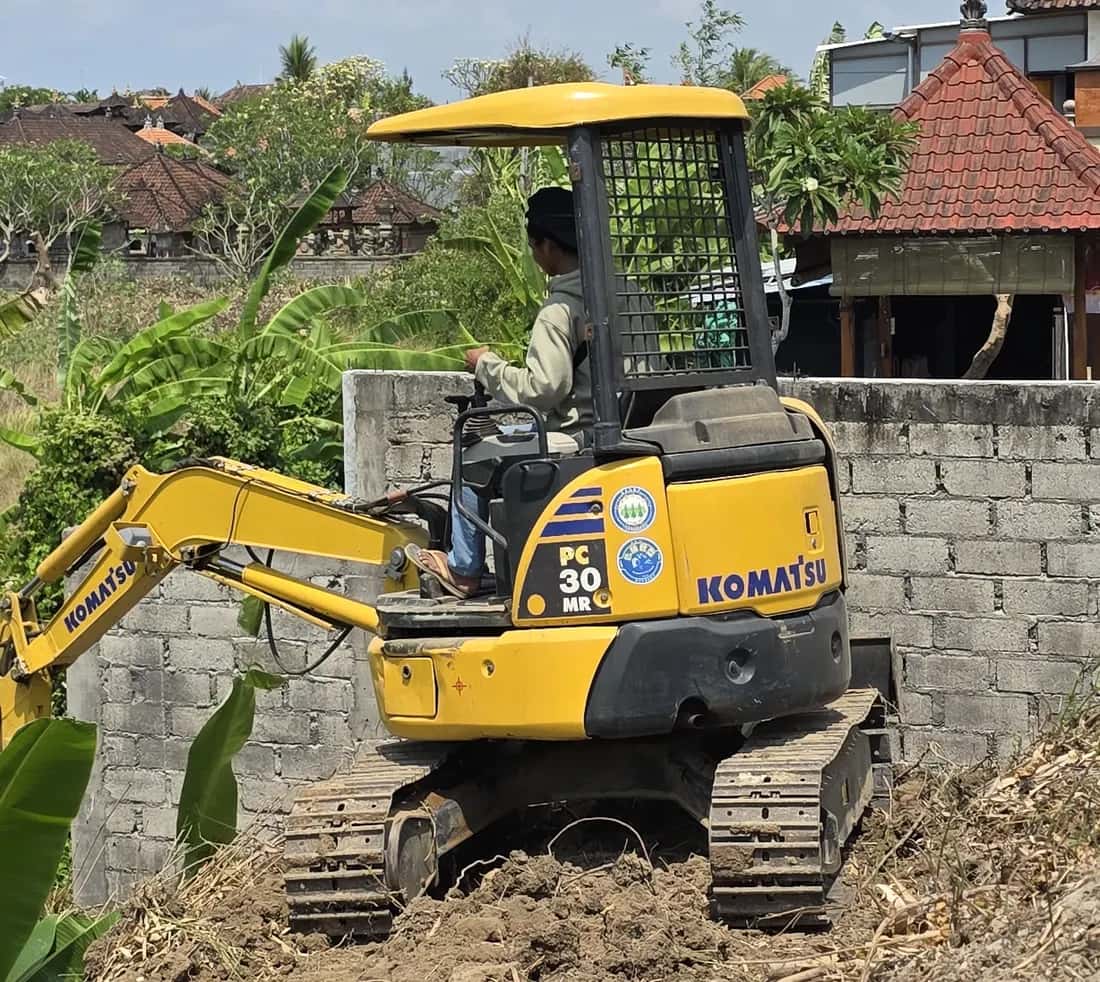 Mini excavator Komatsu PC30MR meratakan tanah di samping tembok bata